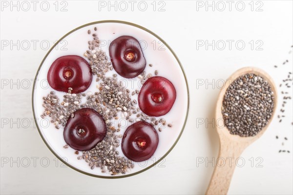 Yoghurt with cherries, chia seeds and granola in glass with wooden spoon on white wooden background. top view, flat lay, close up