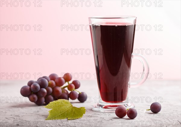 Glass of red grape juice on a gray and pink background. Morninig, spring, healthy drink concept. Side view, close up