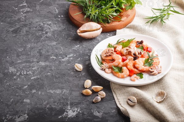 Boiled shrimps or prawns and small octopuses with herbs on white ceramic plate on a black concrete background and linen textile. side view, close up, copy space