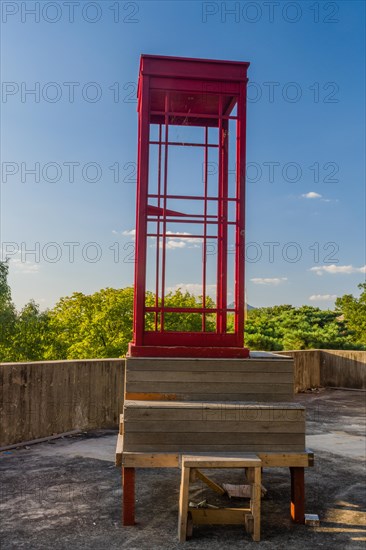 Red wooden telephone booth minus phone and without glass on roof of building on sunny day with blue skies in South Korea