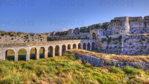 Sunlit view of an old fortress with an aqueduct over green hills, sea fortress Methoni, Peloponnese, Greece, Europe