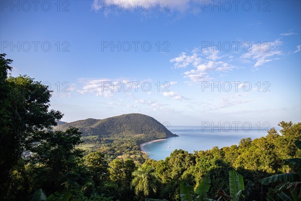 View from a mountain onto an empty sandy beach, the turquoise-coloured sea and the surrounding landscape. The morning sun illuminates the natural surroundings of Grande Anse Beach, Basse Terre, Guadeloupe, the French Antilles and the Caribbean in a unique way at sunrise, North America