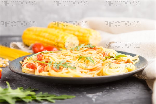 Corn noodles with tomato sauce and arugula on a black concrete background and linen textile. Side view, close up, selective focus