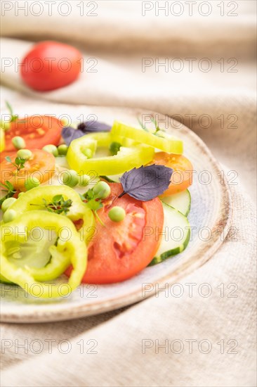 Vegetarian salad from green pea, tomatoes, pepper and basil on white wooden background and linen textile. Side view, close up, selective focus
