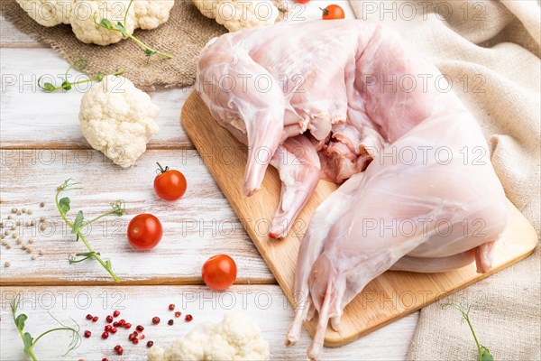 Whole raw rabbit with cauliflower, tomatoes and spices on a white wooden background and linen textile. Side view, close up, selective focus