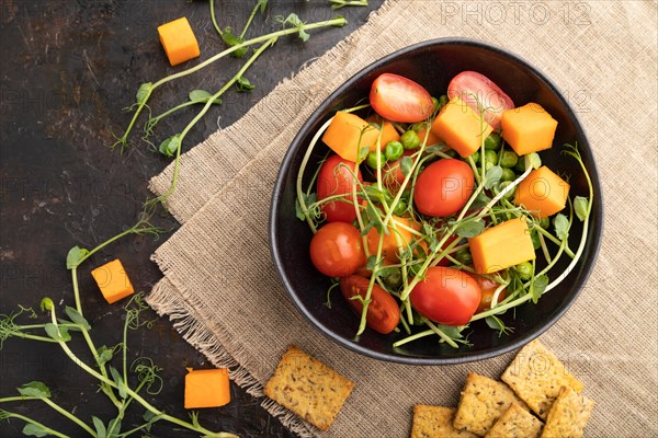 Vegetarian vegetable salad of tomatoes, pumpkin, microgreen pea sprouts on black concrete background and linen textile. Top view, flat lay, close up