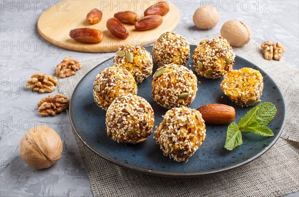 Energy ball cakes with dried apricots, sesame, linen, walnuts and dates with green mint leaves on a blue ceramic plate on a gray concrete background. linen napkin, side view, close up. vegan homemade candy