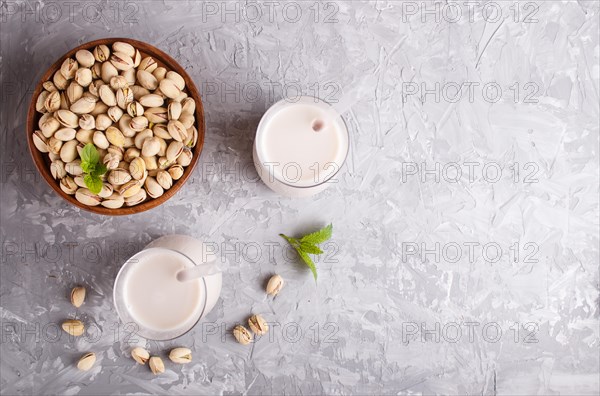 Organic non dairy pistachio milk in glass and wooden plate with pistachionuts on a gray concrete background. Vegan healthy food concept, flat lay, top view, copy space
