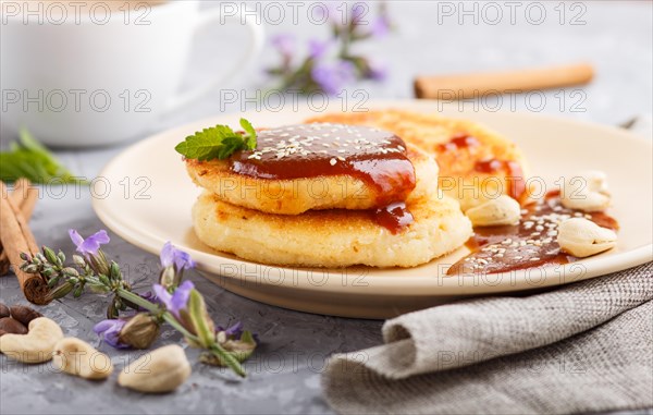 Cheese pancakes with caramel sauce on a beige ceramic plate and a cup of coffee on a gray concrete background. side view, close up