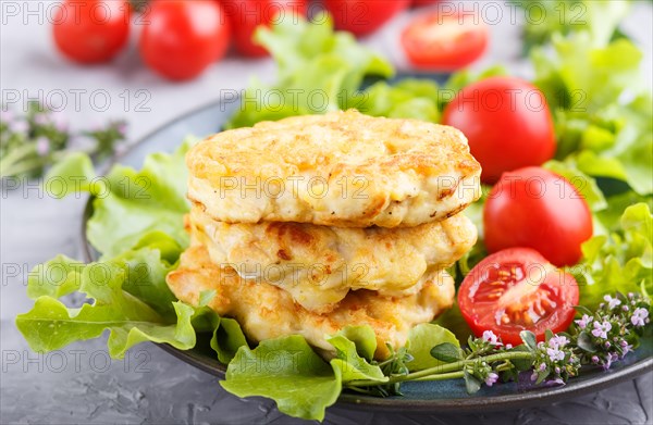 Minced chicken cutlets with lettuce, tomatoes and herbs on a gray concrete background. side view, close up, selective focus