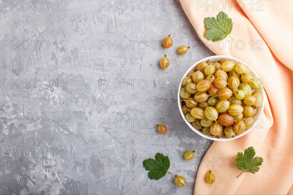 Fresh green gooseberry in white bowl with orange textile on gray concrete background. top view, copy space