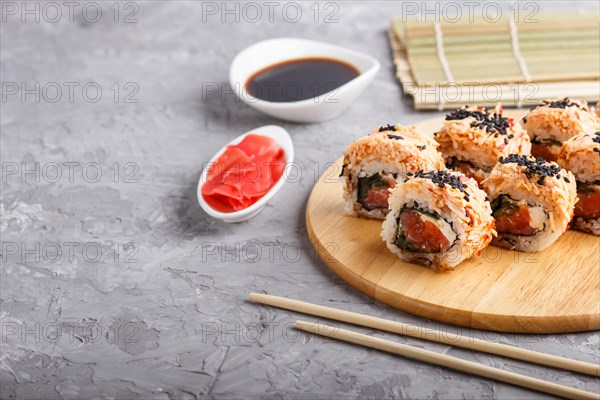 Japanese maki sushi rolls with salmon, sesame, chopsticks, soy sauce and marinated ginger on wooden board on a gray concrete background. Side view, copy space, selective focus