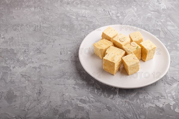 Traditional indian candy soan papdi in white plate with almond and pistache on a gray concrete background. side view, copy space