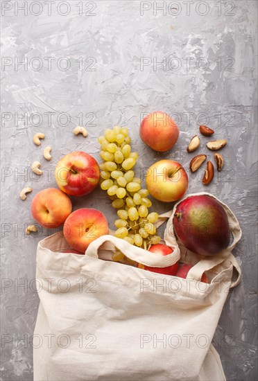 Fruits in reusable cotton textile white bag. Zero waste shopping, storage and recycling concept, eco friendly lifestyle. Top view, flat lay, copy space. Peach, apple, nuts, mango, grape