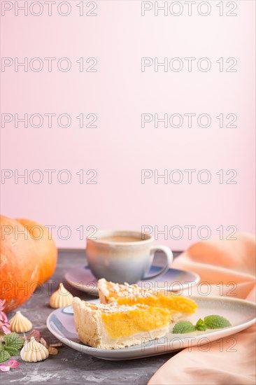 Two pieces of traditional american pumpkin pie with cup of coffee on a black and pink background and orange textile. side view, copy space, contrast
