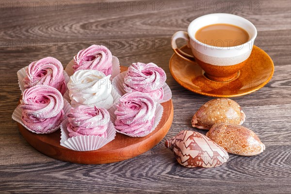 Pink and white homemade marshmallows (zephyr) on a round wooden board with cup of coffee and seashells on a gray wooden background
