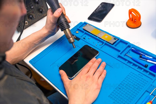 Top view of a technician attaching the parts of a mobile phone using a soldering iron in a workshop