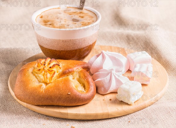 Sweet buns, meringues and coffee cup on a wooden board and linen tablecloth