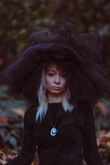 A woman in an oversized hat amidst autumn leaves evokes a moody mystery