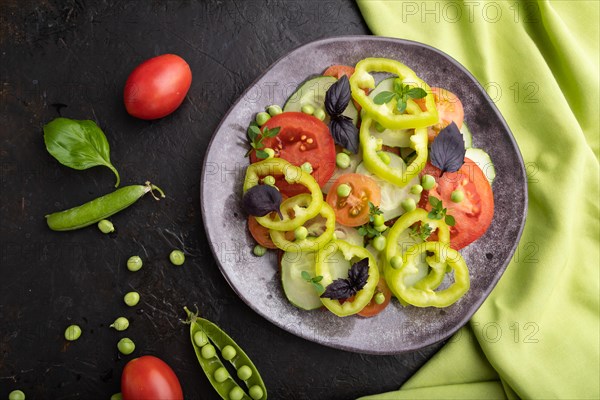 Vegetarian salad from green pea, tomatoes, pepper and basil on a black concrete background and green textile. top view, close up, flat lay