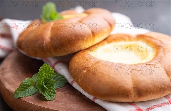 Sour cream bun with cup of coffee on a black concrete background and linen textile. Side view, close up, selective focus