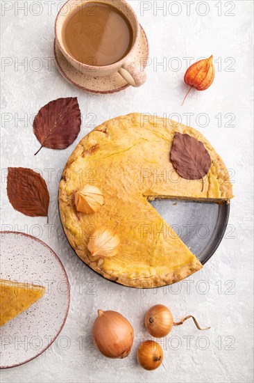 Autumn onion pie decorated with leaves and cup of coffee on gray concrete background. Top view, flat lay, close up