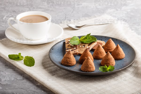 Chocolate truffle on blue ceramic plate and a cup of coffee on gray concrete background. close up, side view