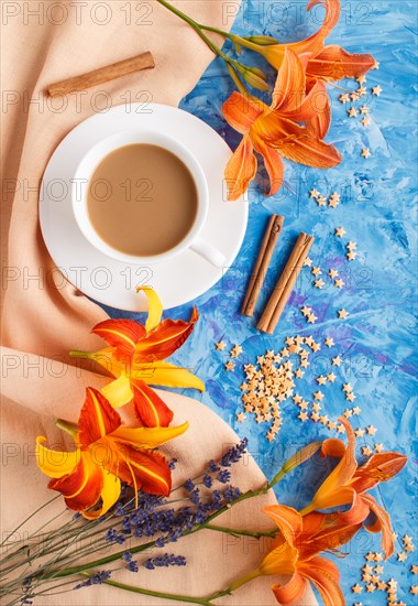 Orange day-lily and lavender flowers and a cup of coffee on a blue concrete background, with orange textile. Morninig, spring, fashion composition. Flat lay, top view, close up