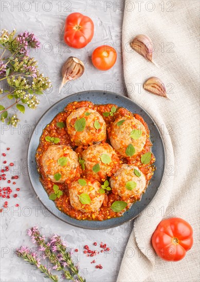 Pork meatballs with tomato sauce, oregano leaves, spices and herbs on blue ceramic plate on a gray concrete background with linen textile. top view, flat lay, close up
