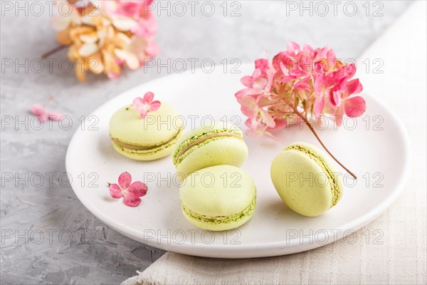 Green macarons or macaroons cakes on white ceramic plate on a gray concrete background and linen textile. side view, close up, selective focus