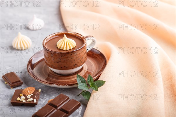 Cup of hot chocolate and pieces of milk chocolate with almonds on a gray concrete background with orange textile. side view, copy space