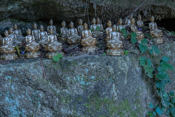 Miniature sitting Buddhas on ledge of boulder in mountainous public park in South Korea