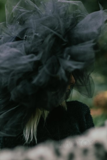Side view of a woman in a large tulle hat, partially obscured by a blurred foreground