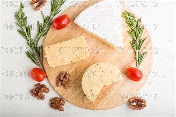Cheddar and various types of cheese with rosemary and tomatoes on wooden board on a white wooden background. Top view, flat lay, close up