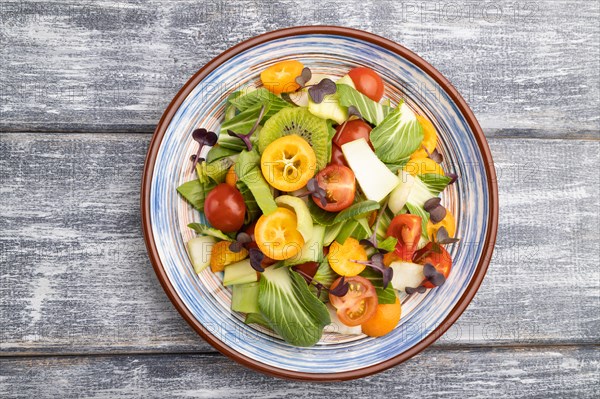 Vegetarian salad of pac choi cabbage, kiwi, tomatoes, kumquat, microgreen sprouts on gray wooden background. Top view, flat lay, close up