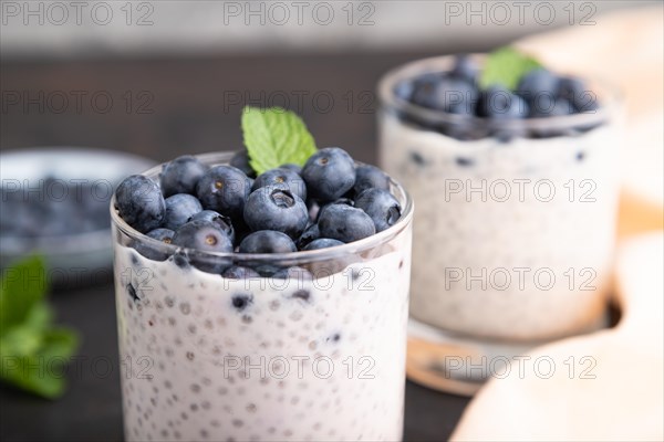 Yogurt with blueberry and chia in glass on black concrete background and orange linen textile. Side view, close up