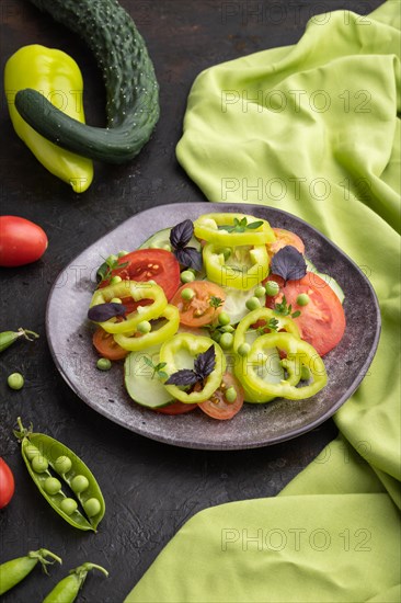Vegetarian salad from green pea, tomatoes, pepper and basil on a black concrete background and green textile. Side view, close up