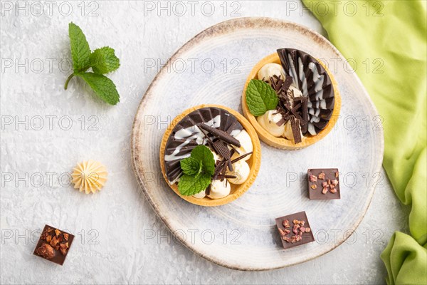 Sweet tartlets with chocolate and cheese cream with cup of coffee on a gray concrete background and green textile. top view, flat lay, close up