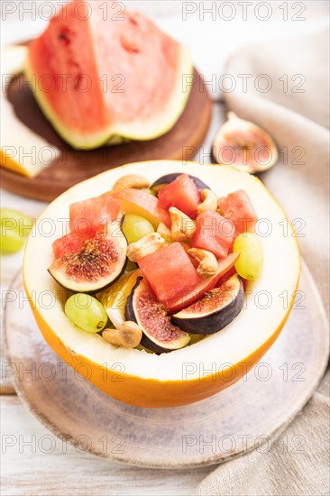 Vegetarian fruit salad of watermelon, grapes, figs, pear, orange, cashew on white wooden background and linen textile. Side view, close up, selective focus