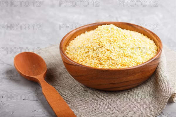Wooden bowl with cornflakes and a wooden spoon on a gray concrete background. linen napkin, side view, close up