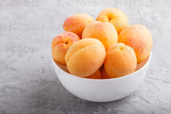 Fresh orange apricots in white bowl on gray concrete background. side view, close up, selective focus