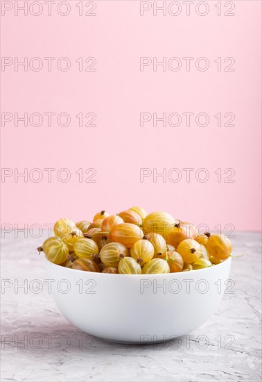 Fresh green gooseberry in white bowl on gray and pink background. side view, copy space