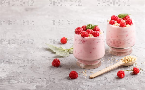 Yoghurt with raspberry and sesame in a glass and wooden spoon on gray concrete background. side view, copy space, selective focus
