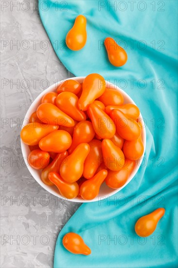Fresh orange grape tomatoes in white ceramic bowl on gray concrete background with blue textile. top view, flat lay, close up