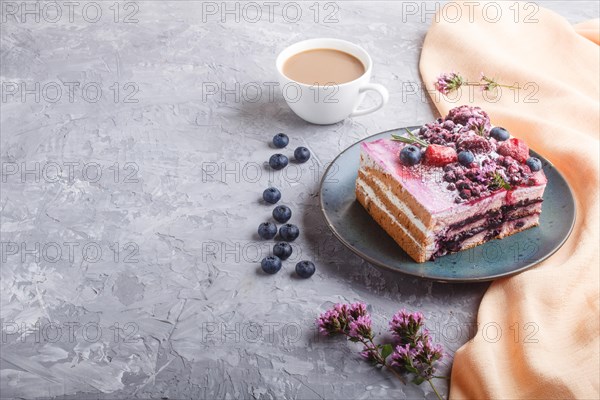 Berry cake with milk cream and blueberry jam on blue ceramic plate with cup of coffee and fresh blueberries on a gray concrete background with orange textile. side view, copy space