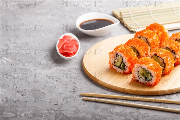Japanese maki sushi rolls with flying fish roe, chopsticks, soy sauce and marinated ginger on wooden board on a gray concrete background. Side view, copy space, selective focus