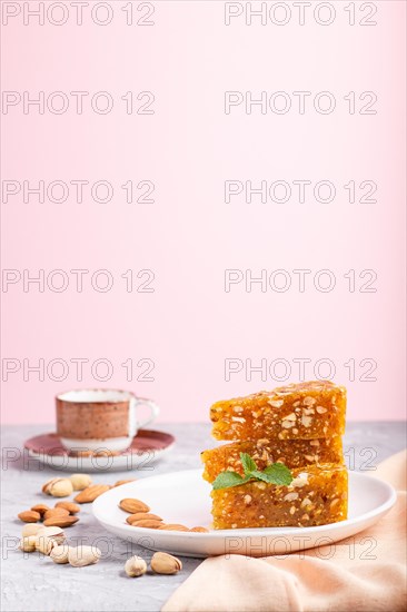 Traditional turkish candy cezerye made from caramelised melon, roasted walnuts, hazelnuts, cashew, pistachios on white ceramic plate and a cup of coffee on a gray and pink background. side view, close up