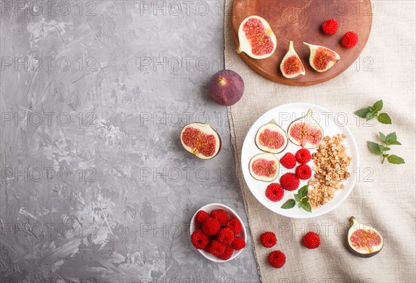 Yoghurt with raspberry, granola and figs in white plate on a gray concrete background and linen textile. top view, flat lay, copy space