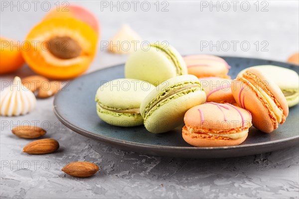 Orange and green macarons or macaroons cakes on blue ceramic plate on a gray concrete background. side view, close up, selective focus