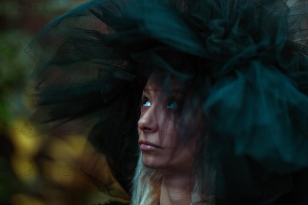 Close-up of a contemplative white thin caucasian blonde woman's face with a big, fluffy tulle hat